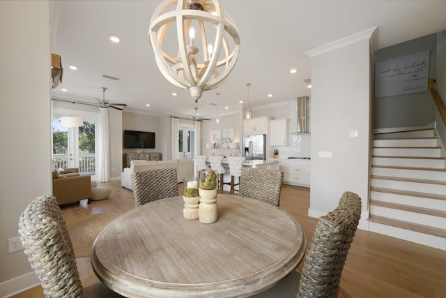 dining space featuring ornamental molding, ceiling fan with notable chandelier, and light hardwood / wood-style flooring