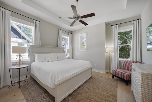 bedroom with light wood-type flooring, ceiling fan, and a raised ceiling