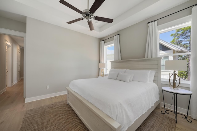 bedroom with ceiling fan, light hardwood / wood-style flooring, and a raised ceiling