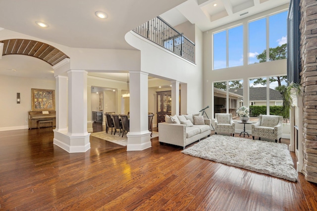 living room with coffered ceiling, a high ceiling, decorative columns, and dark wood-type flooring