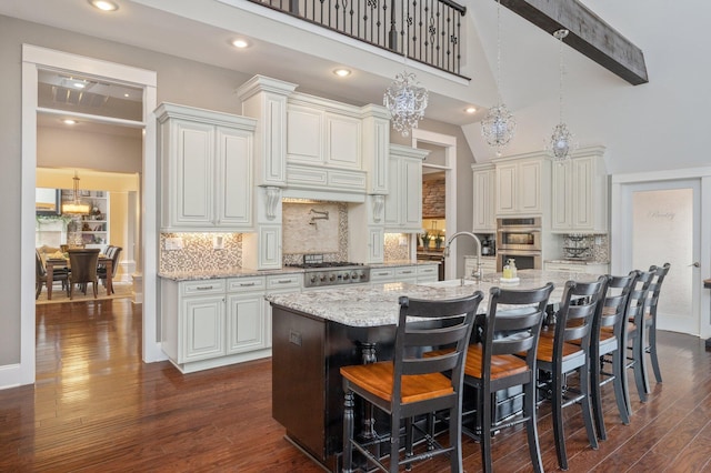 kitchen featuring light stone countertops, high vaulted ceiling, a kitchen island with sink, a breakfast bar area, and sink