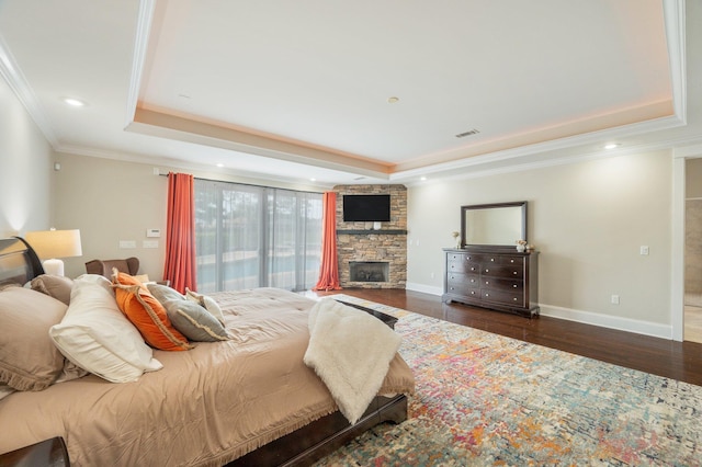 bedroom featuring a raised ceiling, ornamental molding, dark hardwood / wood-style flooring, and a stone fireplace