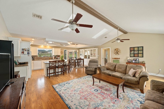 living room featuring ceiling fan, vaulted ceiling with beams, and light wood-type flooring