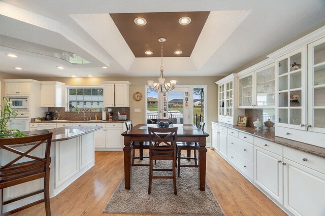 dining area featuring light hardwood / wood-style floors, an inviting chandelier, a raised ceiling, and sink