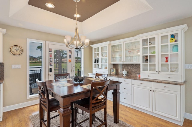 dining room with light hardwood / wood-style floors, a notable chandelier, and a raised ceiling