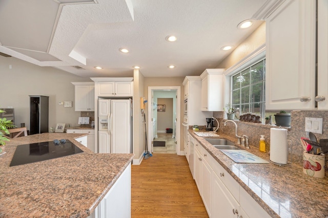 kitchen with paneled built in refrigerator, tasteful backsplash, black electric cooktop, white cabinets, and sink