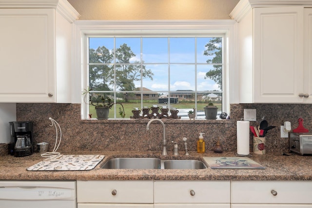 kitchen featuring a healthy amount of sunlight, tasteful backsplash, white cabinetry, white dishwasher, and sink