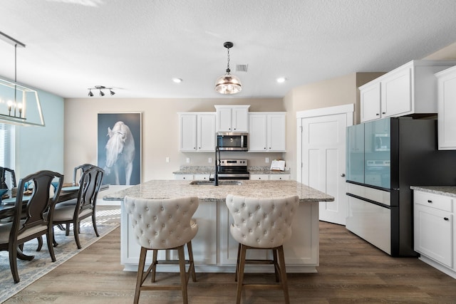 kitchen featuring white cabinetry, hanging light fixtures, a center island with sink, and stainless steel appliances