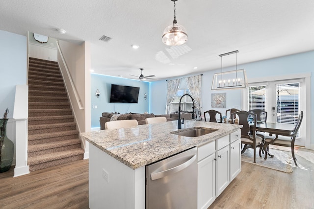 kitchen featuring stainless steel dishwasher, sink, white cabinetry, hanging light fixtures, and a kitchen island with sink