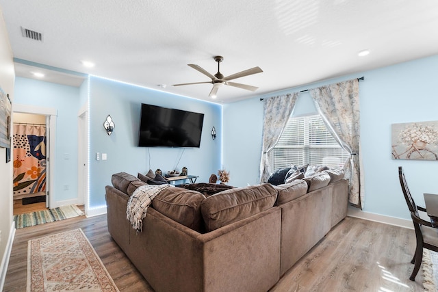 living room featuring light wood-type flooring, ceiling fan, and a textured ceiling