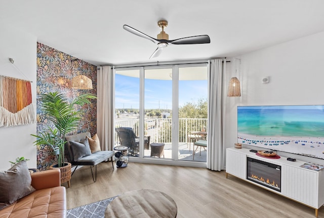 living room with ceiling fan, a wall of windows, and light wood-type flooring