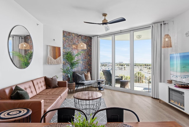 living room with ceiling fan, a wall of windows, and light hardwood / wood-style floors