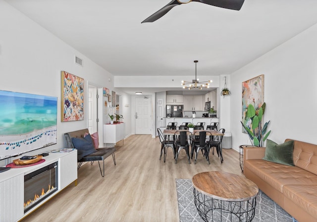 living room featuring ceiling fan with notable chandelier and light wood-type flooring