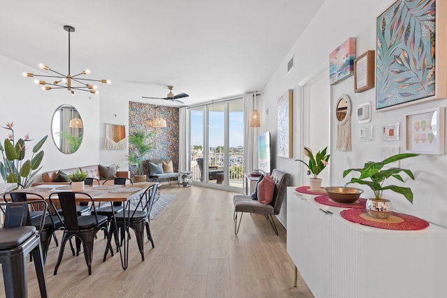 dining area with a wall of windows, ceiling fan with notable chandelier, and light wood-type flooring