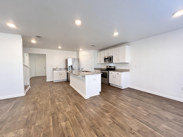 kitchen with sink, white cabinets, stainless steel appliances, light stone countertops, and a center island with sink