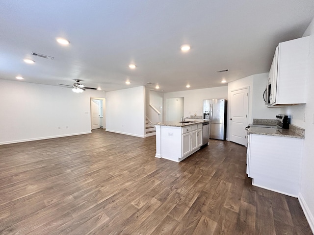 kitchen with dark hardwood / wood-style floors, white cabinetry, stainless steel appliances, light stone countertops, and a center island with sink