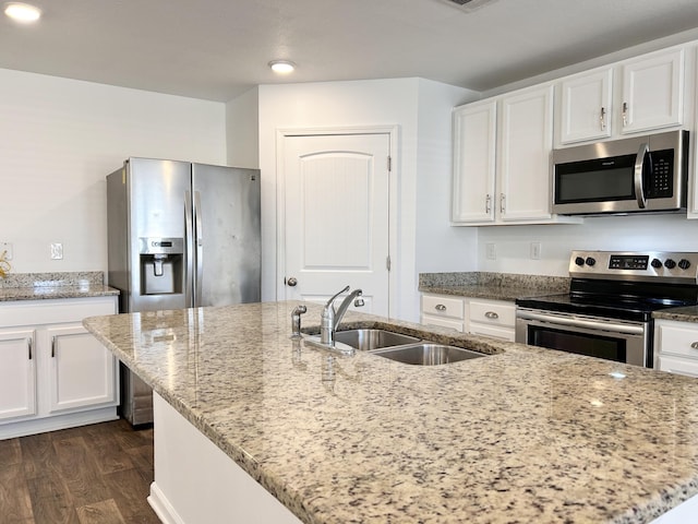 kitchen with light stone countertops, appliances with stainless steel finishes, sink, and a center island with sink