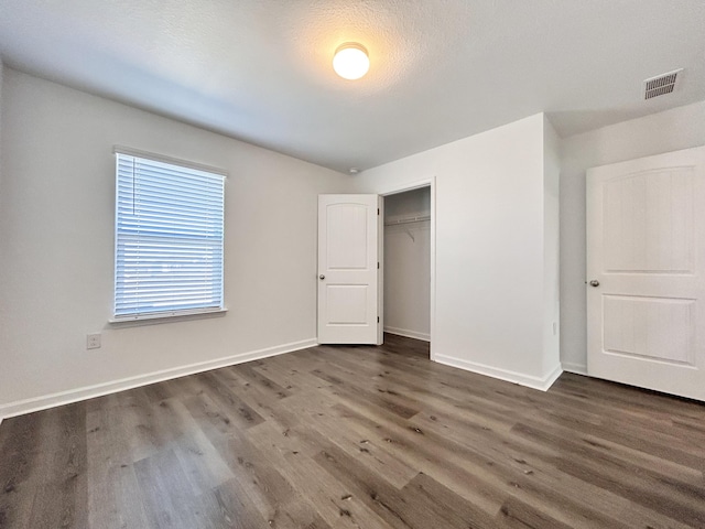 unfurnished bedroom featuring dark wood-type flooring, a textured ceiling, and a closet