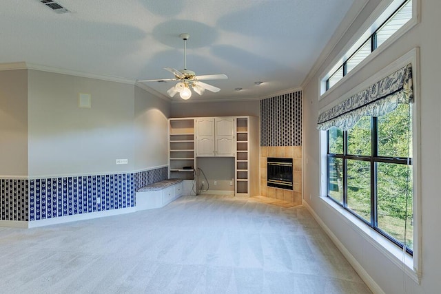 unfurnished living room featuring a wealth of natural light, light carpet, ceiling fan, a tile fireplace, and crown molding