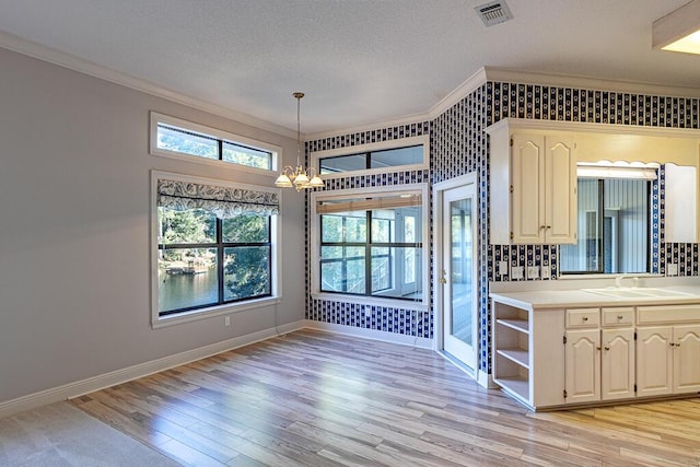 kitchen featuring pendant lighting, sink, light wood-type flooring, ornamental molding, and a chandelier