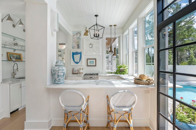 bar featuring white cabinetry, hanging light fixtures, light stone countertops, sink, and light hardwood / wood-style flooring