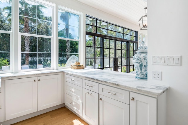 interior space with decorative light fixtures, white cabinetry, an inviting chandelier, light stone counters, and light hardwood / wood-style floors