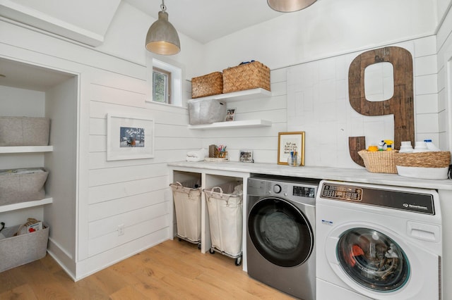 laundry area featuring washing machine and clothes dryer, wood walls, and light hardwood / wood-style floors