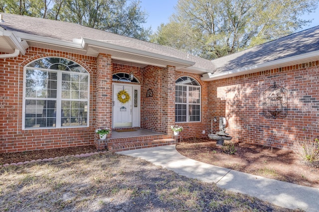 entrance to property featuring brick siding and roof with shingles