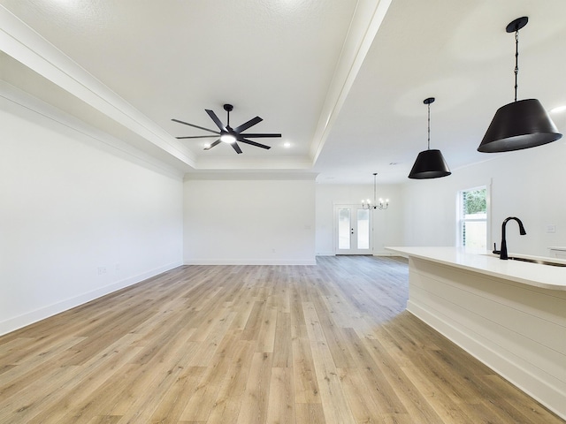 unfurnished living room with a raised ceiling, crown molding, light wood-style flooring, and a sink