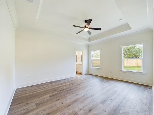 spare room featuring a raised ceiling, crown molding, baseboards, and wood finished floors