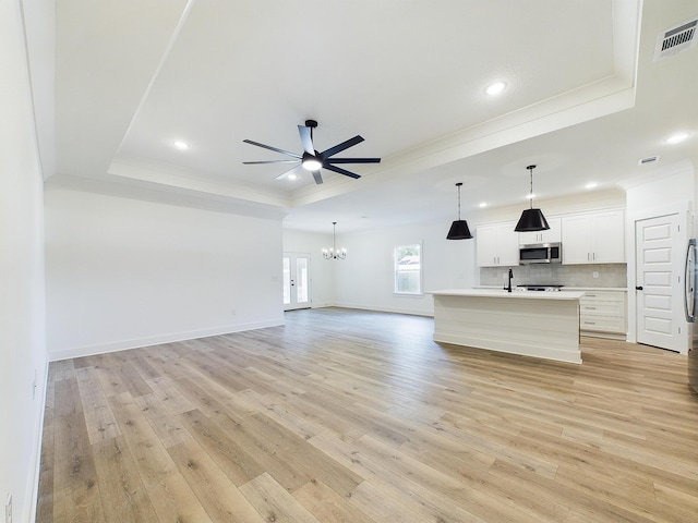 unfurnished living room featuring ceiling fan with notable chandelier, visible vents, ornamental molding, a tray ceiling, and light wood finished floors