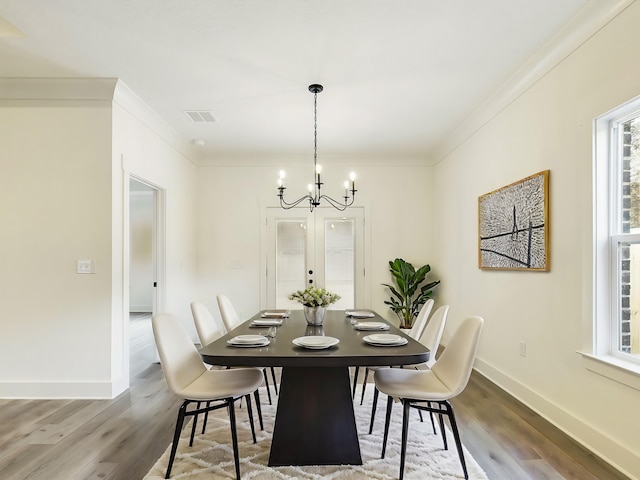 dining space with crown molding, visible vents, a notable chandelier, and wood finished floors