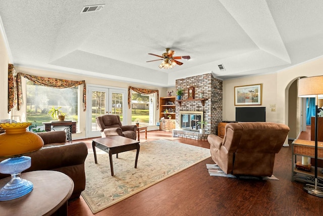 living room with ceiling fan, a brick fireplace, a raised ceiling, and dark wood-type flooring