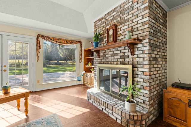 living room featuring a textured ceiling, a fireplace, hardwood / wood-style flooring, ornamental molding, and vaulted ceiling