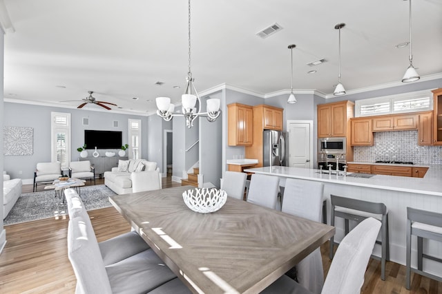 dining space with ceiling fan with notable chandelier, light hardwood / wood-style flooring, a healthy amount of sunlight, and sink