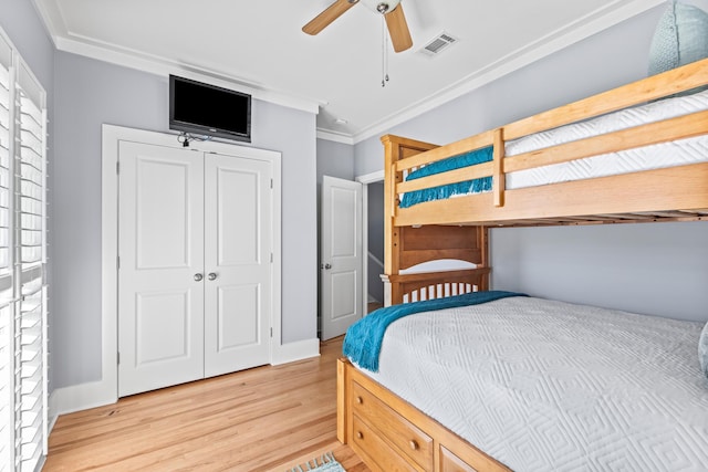 bedroom with light wood-type flooring, ceiling fan, crown molding, and a closet