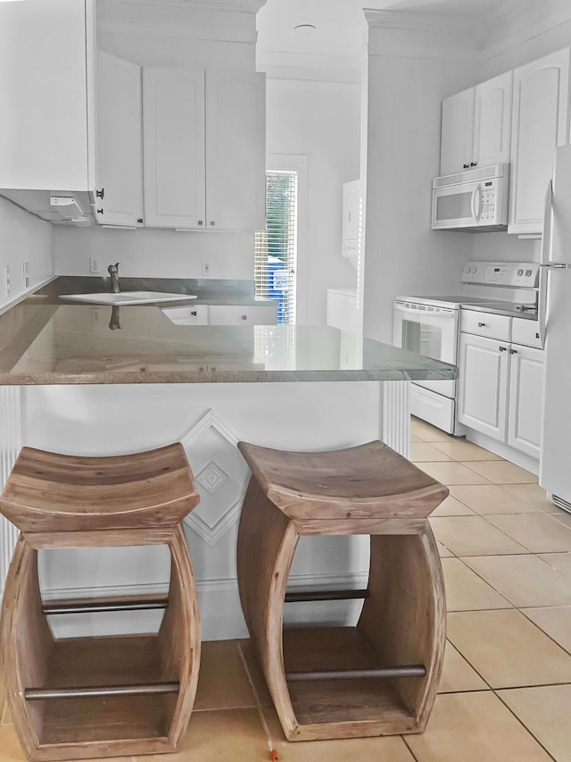 kitchen featuring a breakfast bar area, white appliances, white cabinetry, and light tile patterned floors