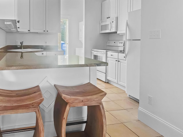 kitchen featuring white appliances, kitchen peninsula, light tile patterned floors, white cabinets, and sink