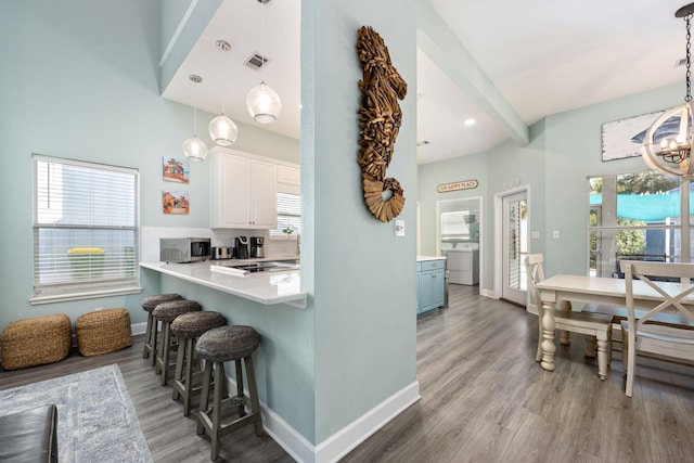 kitchen featuring a kitchen bar, decorative light fixtures, hardwood / wood-style flooring, washer / clothes dryer, and white cabinets