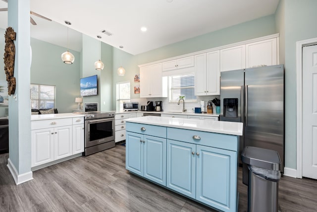 kitchen featuring blue cabinetry, sink, hanging light fixtures, stainless steel appliances, and white cabinets