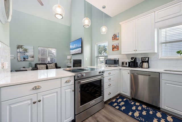 kitchen featuring decorative light fixtures, white cabinets, decorative backsplash, kitchen peninsula, and stainless steel appliances