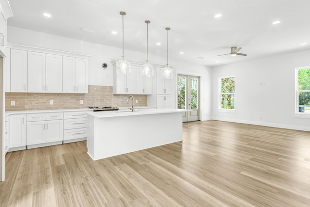 kitchen with pendant lighting, a center island with sink, light hardwood / wood-style floors, white cabinetry, and ceiling fan