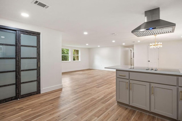 kitchen featuring island range hood, gray cabinets, black electric stovetop, light wood-type flooring, and pendant lighting