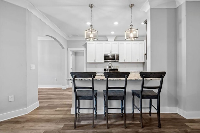 kitchen with crown molding, a kitchen bar, light stone counters, white cabinets, and decorative light fixtures