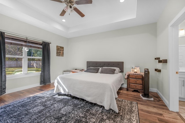 bedroom featuring ceiling fan, wood-type flooring, and a tray ceiling