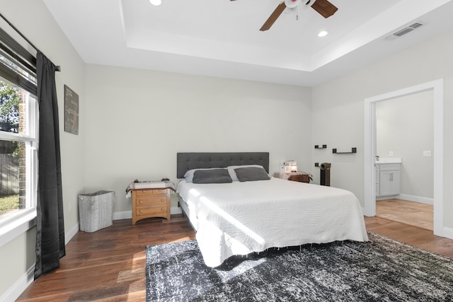 bedroom featuring ensuite bath, ceiling fan, a tray ceiling, and dark hardwood / wood-style flooring