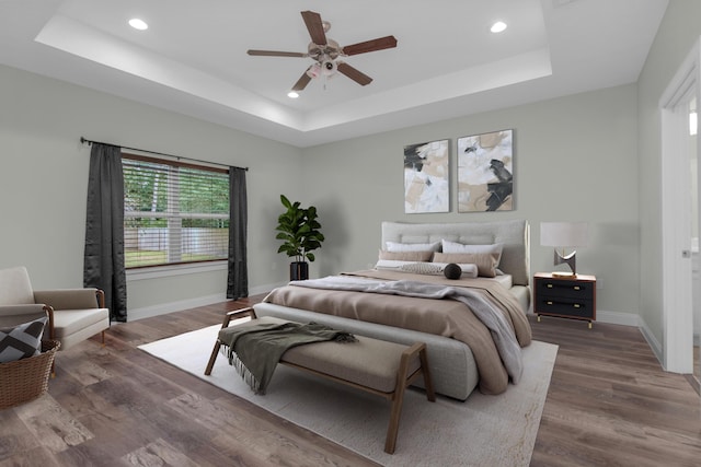 bedroom with dark wood-type flooring, recessed lighting, a raised ceiling, and baseboards