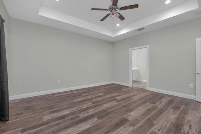 unfurnished room featuring a tray ceiling, dark wood finished floors, recessed lighting, visible vents, and baseboards