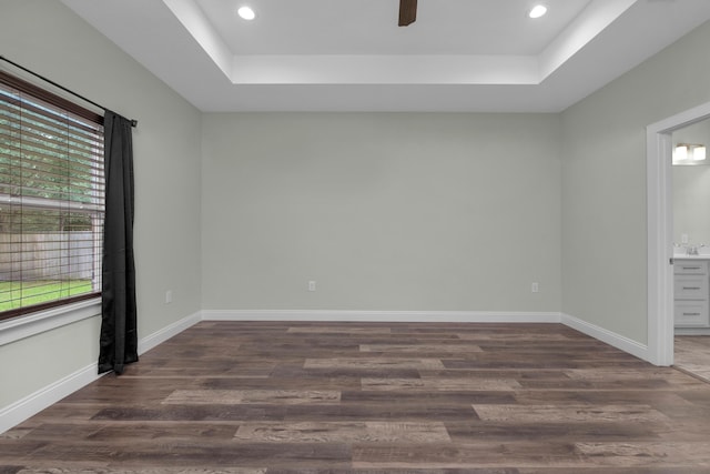 unfurnished room featuring a raised ceiling, dark wood finished floors, and baseboards