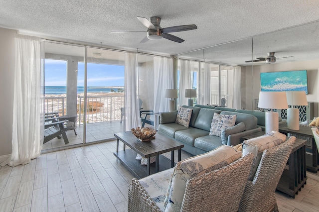 living room featuring a textured ceiling, ceiling fan, expansive windows, and a water view